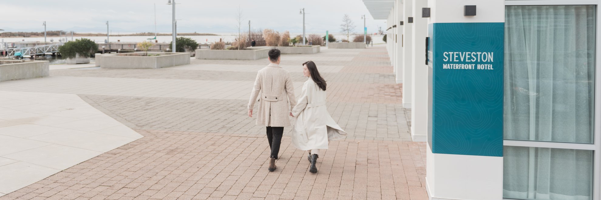 couple holding hands walking down the Steveston waterfront in front of the hotel